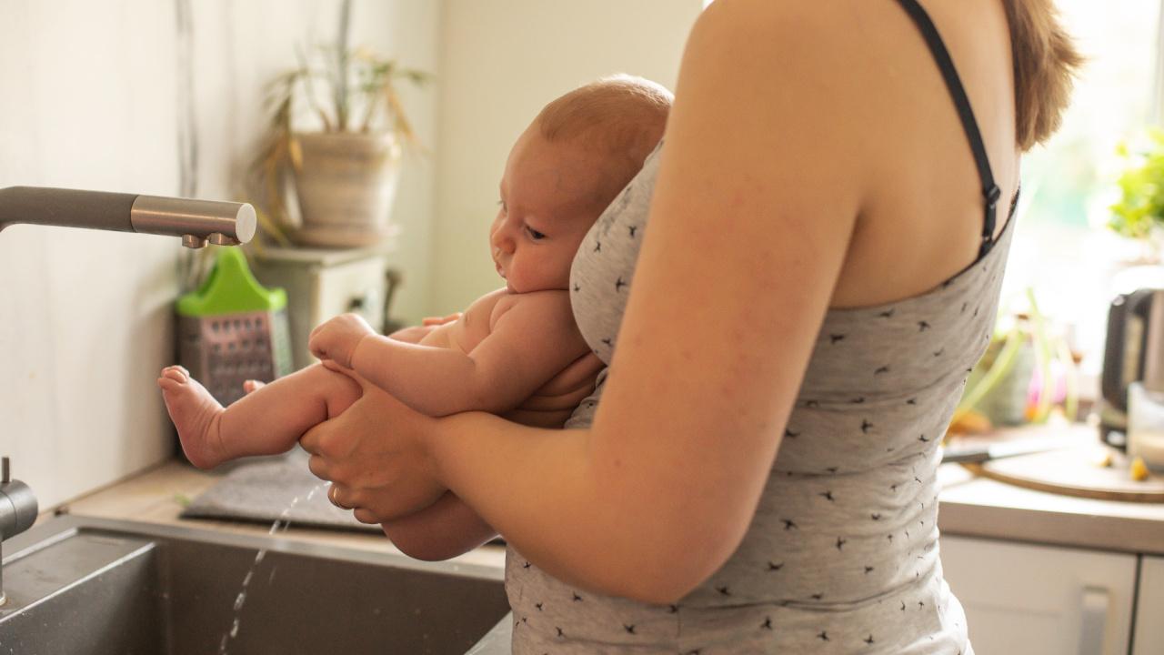 Natūralioji higiena - mama laiko besišlapinantį kūdikį virš kriauklės.
