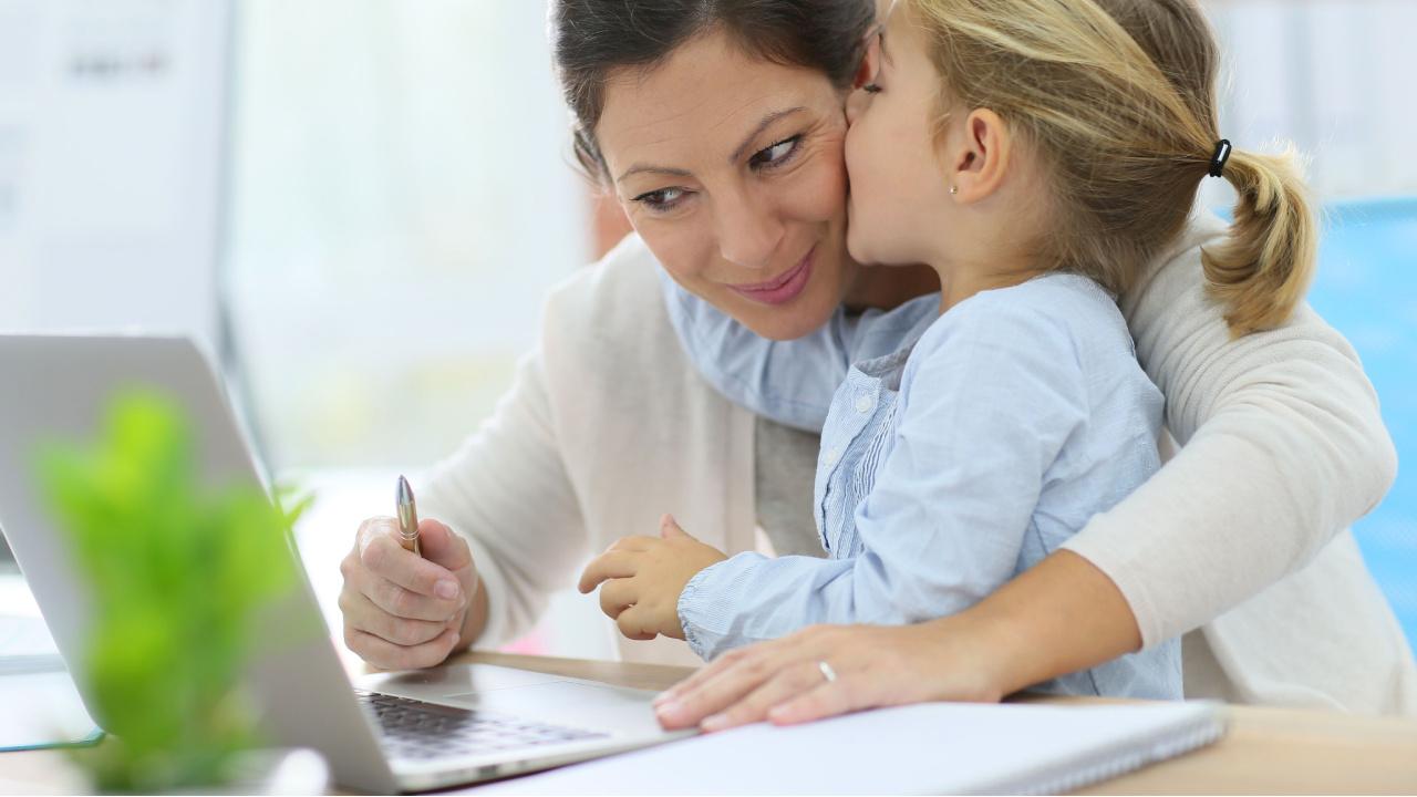 Mergaitė su prie kompiuterio dirbančia mama