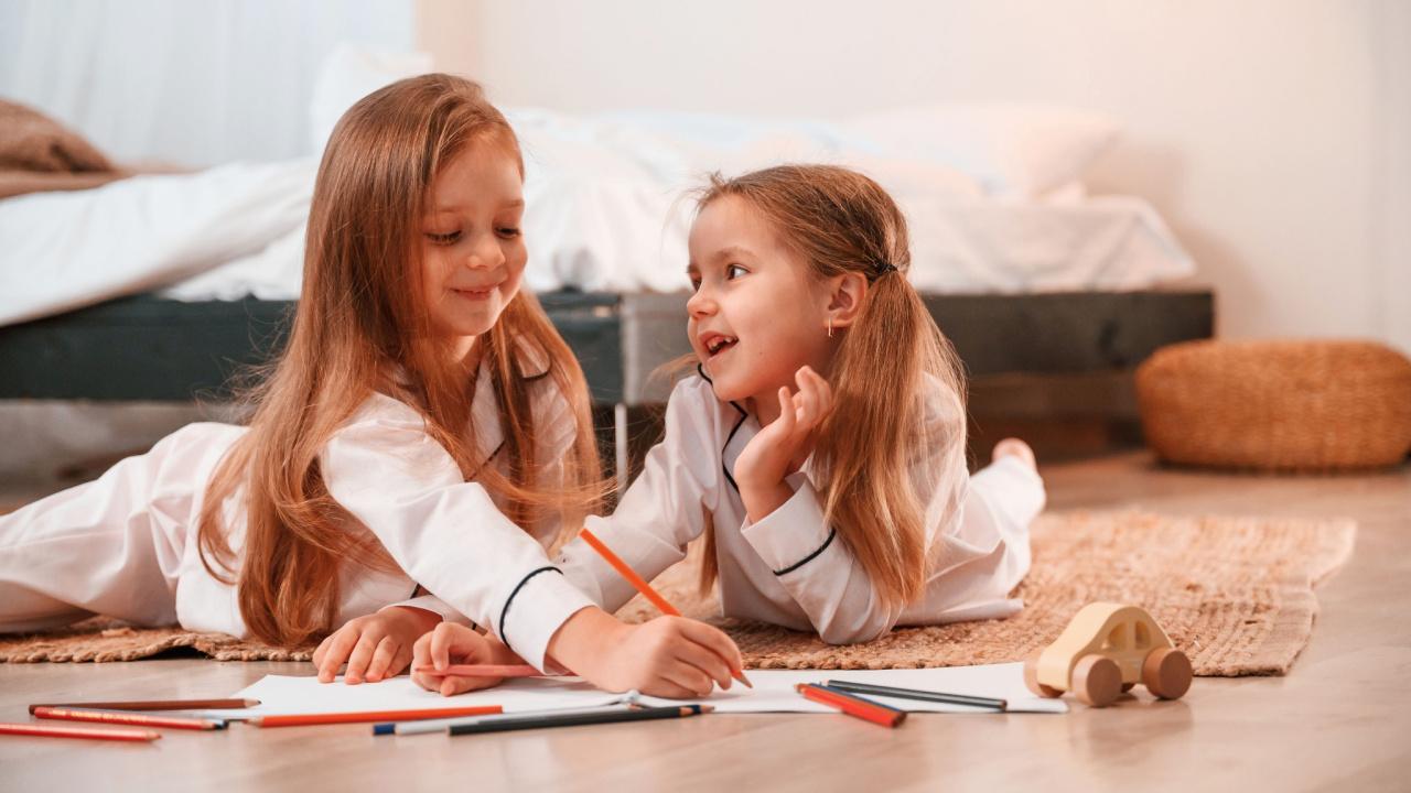 Mergaitės guli ant grindų, piešia ir kalbasi