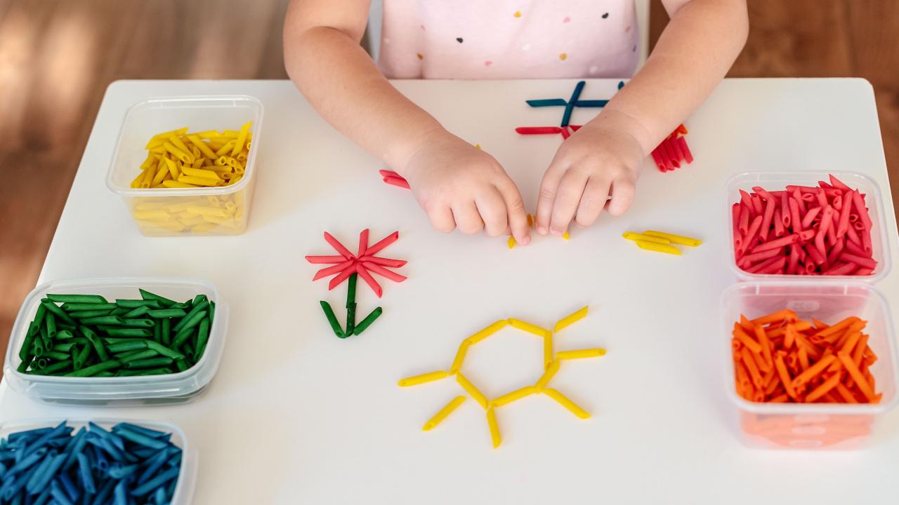 Mergaitė dėlioja piešinėlius iš makaronų